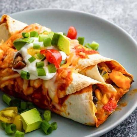 A plate of vegetarian enchiladas topped with avocado and sour cream