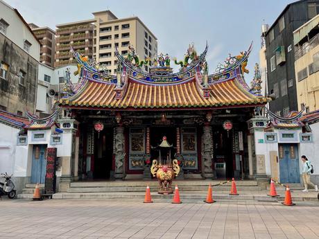 20 Best Places to Visit in Taiwan A traditional Taiwanese temple with a detailed, colorful rooftop featuring statues of dragons and deities, framed by modern apartment buildings in the background.