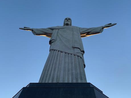 Looking up at the christ the redeemer statue in rio de janeiro from the base of the plinth. The statue fills the shot and the sky is deep blue beyond.