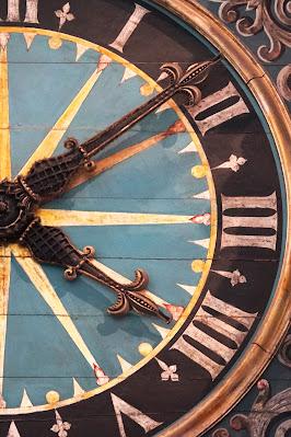 Illustrative photo showing part of a clock face, painted with roman numerals and including two ornate clock hands.