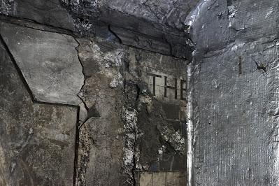 Hidden signs of Green Park station On a dirty wall, the word 'THE' is visible on cream tiles. To the right, a wall stands at right angles to it.
