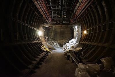 Hidden signs of Green Park station A dark tunnel lined with iron panels. At the end, lights are on, showing stored sacks and a short flight of steps to one side.