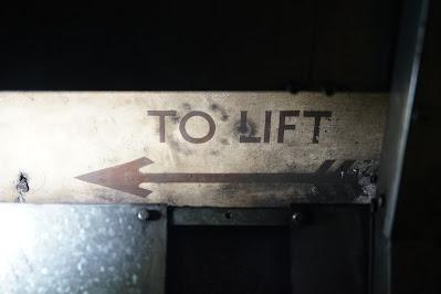 Hidden signs of Green Park station Against a dark background, a cream panel has 'TO LIFT' and an arrow painted on it in dark brown.