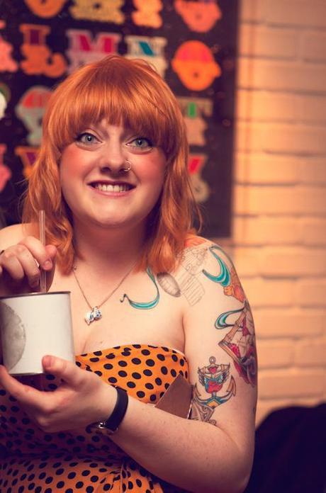 A heavily tattooed woman smiles and drinks coffee