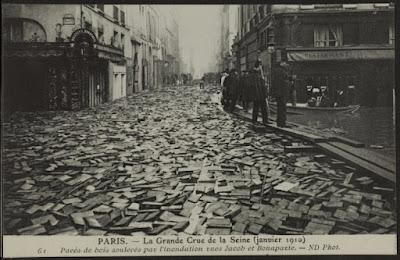 Vintage postcard showing a street surface littered with many loose wooden blocks.
