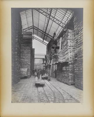 Vintage photo of a glass-roofed warehouse filled with large, high piles of wooden blocks