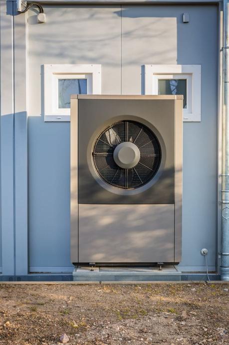 Grey air source heat pump in front of house