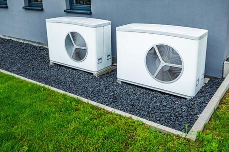 A home owner’s guide to heat pump maintenance Pair of white air source heat pumps installed outside modern property on gray gravel nearby grass lawn