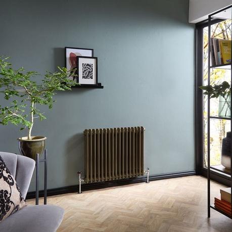 A guide to radiator repair and replacement costs Milano Windsor metallic bronze horizontal traditional double column radiator on blue wall beneath artwork nearby small table with plant