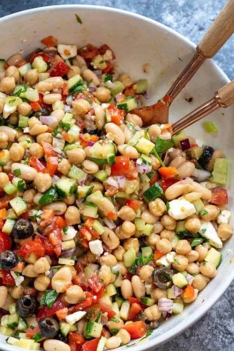 an overhead shot of a bean salad in a white bowl with tongs