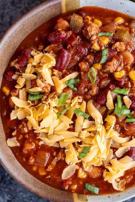 a closeup shot of turkey chili in a bowl with shredded cheese
