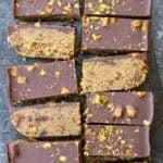 Eleven pistachio bars sliced on the counter, topped with dark chocolate and chopped nuts
