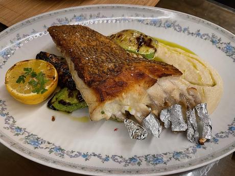 The Albanian Riviera: Best Beaches, Towns, and Hidden Gems Grilled fish fillet served with lemon, courgette, and smooth purée on a floral plate. A refined take on Albanian coastal cuisine highlighting the country’s fresh seafood.