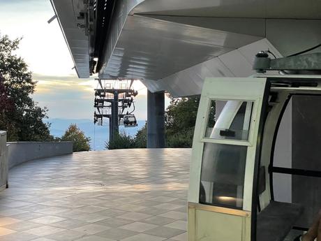 Cable car cabins of the Dajti Ekspres gliding down the mountain as the sun sets over Tirana. A peaceful moment showing the start of the descent with distant views of the hills and valley below.