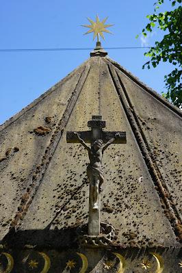 Photo showing detail of the mausoleum including a row of gold crescents, a carved crucifix and, at the top of the structure, a gold sun.