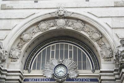 Surprise lion! Photo of the top of a pale stone arched entrance, highly decorated with carving and a semicircular stained glass window.
