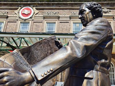 Photo showing a side view of the bronze Thomas Brassey statue. In the foreground is his left hand holding a map.