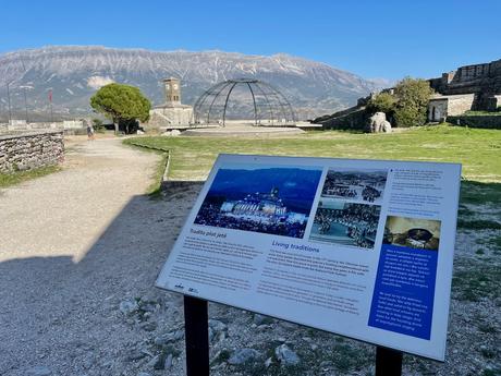 Informational sign inside Gjirokaster Castle explaining the city’s living traditions, with stone walls, a clock tower, and mountains in the background. A key stop when exploring Gjirokaster attractions and learning about the region’s cultural heritage.