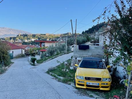 Steep residential street in Gjirokastër, Albania, with a yellow Audi parked beside a stone wall and a view of the city’s castle in the distance. A typical example of Albania’s hilly roads and informal parking common in smaller towns.