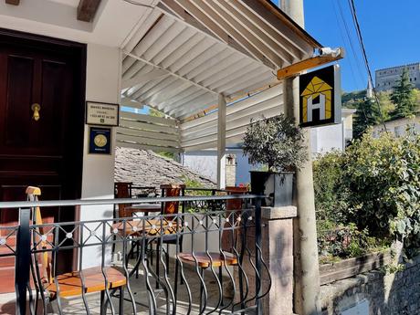 Entrance and terrace of Hotel Domino in Gjirokaster with outdoor seating and a high rating sign from Booking.com. A welcoming stay option for travelers exploring the best places to visit in Gjirokaster.