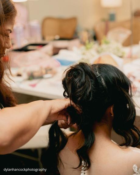 An Emerald & Sage, Zero-Alcohol Real Wedding a bride in a white lace gown sits calmly as her mother carefully styles her hair before the wedding dylanhancockphotography