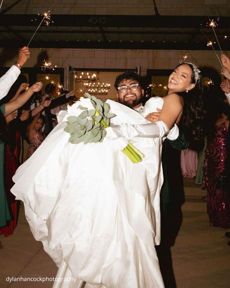An Emerald & Sage, Zero-Alcohol Real Wedding groom carries bride through guests holding sparklers dylanhancockphotography