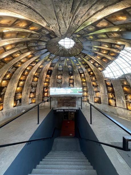 The entrance to Bunk’Art 2, a historical museum in Tirana, Albania, featuring a dramatic underground passage. The curved ceiling is lined with haunting black-and-white portraits of victims of the communist regime.
