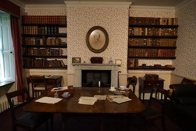 A long way from home - in Bronte country Photo of the Bronte parsonage interior. A room holds a large table scattered with papers; behind are two full bookcases. In the center is a fireplace with an oval picture of Charlotte Bronte hanging above it.