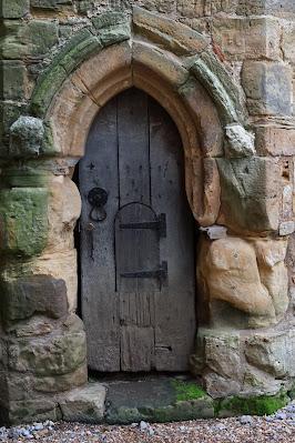 Weathered and worn: Battle Abbey's stones Photo of an old wooden door; the surrounding stone archway has eroded into irregular, curved shapes.