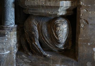 Photo of a strange carving with a cowled human head but the body and rear legs of an animal.