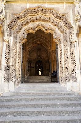 Photo: a flight of stone steps leads to an archway of elaborately carved pale golden stone with a distinctive cinquefoil shape. Beyond it, another arched entrance is visible.