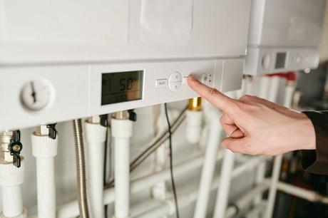Close-up image of a hand pressing button on a white boiler system with white pipes emerging from the bottom