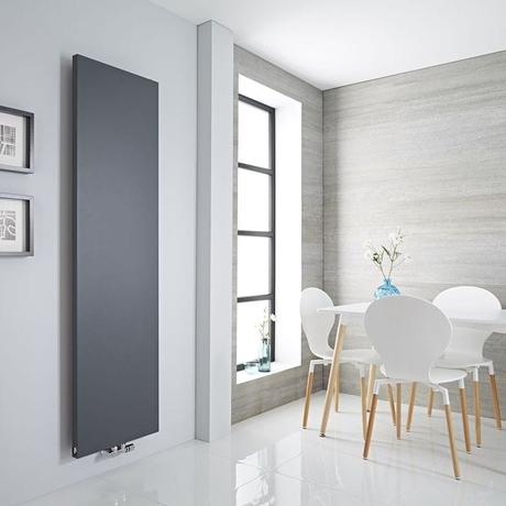 Milano Riso anthracite flat panel vertical designer radiator on white wall nearby framed pictures and white table and chairs and long window by light gray wall