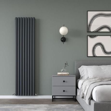 Milano Aruba Ayre anthracite aluminum vertical designer radiator on green wall nearby small gray drawers next to bed beneath framed artwork in modern bedroom