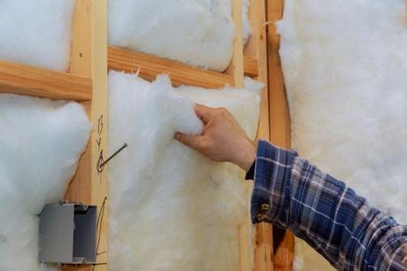 Worker applying rock insulation to walls in house