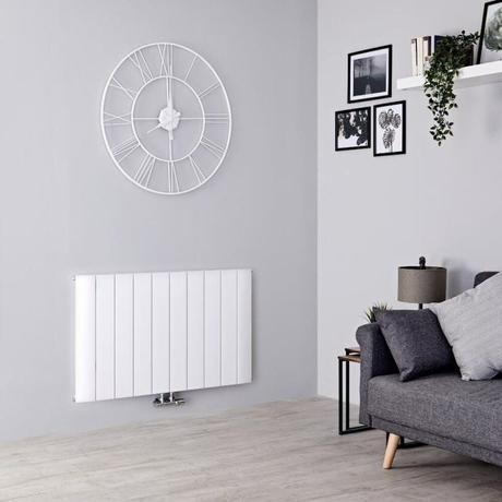 Milano Skye white horizontal alauminium designer radiator on light wall beneath large white clock nearby gray settee and multiple framed pictures near white shelf