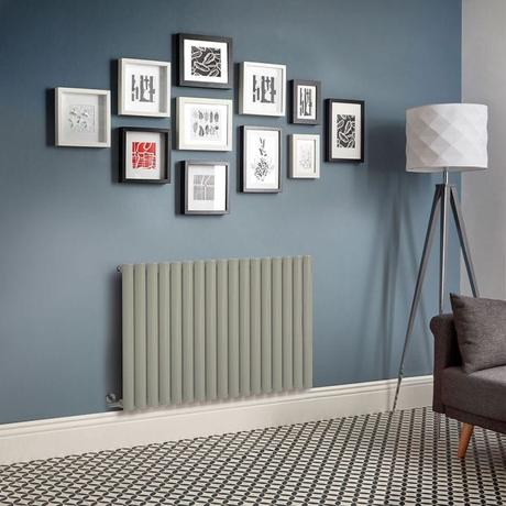Milano Aruba electric sage leaf green horizontal designer radiator on blue wall beneath multiple framed pictures and nearby lamp and charcoal settee