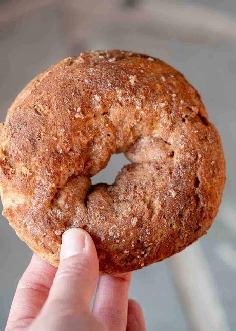a single cinnamon protein bagel being held up with hand in corner of image