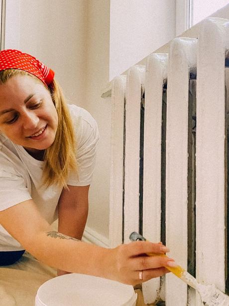 Blonde woman with red spotted bandana painting a white radiator in a home