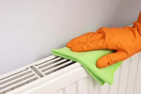 Green cloth being used by hand in orange rubber glove to clean white convector radiator