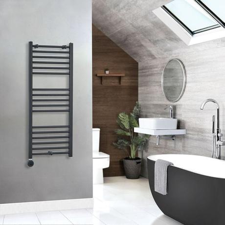 Milano x ECOSO Artle electric curved anthracite heated towel rail on gray wall in modern bathroom setting nearby black and white freestanding tub with chrome tub filler and circular mirror above white sink on floating white shelf