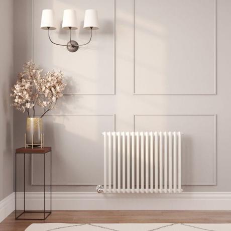 Milano Windsor white traditional horizontal electric double column radiator on white wall nearby small table with gold vase and fake houseplant beneath triple light fitting