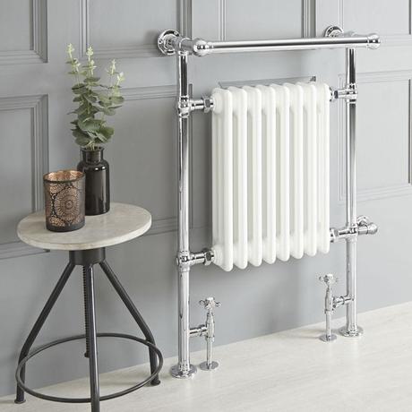 Milano Elizabeth white traditional dual fuel heated towel rail on light gray wall nearby small table with vase and fake houseplant