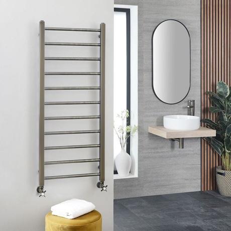 Milano Ezra dark gold stainless steel flat heated towel rail on light wall nearby beige floating shelf with white sink beneath round mirror