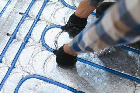 Blue pipes for radiant underfloor heating system being installed on flooring by man with black gloves