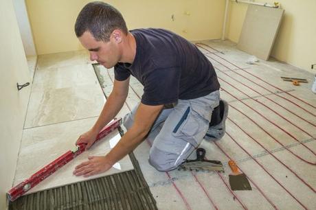 Male worker installing white ceramic tiles over underfloor heating system