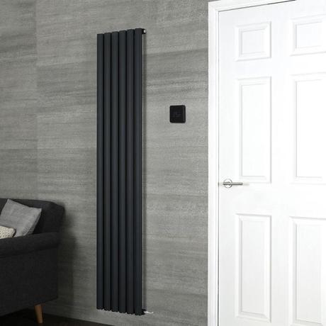 Milano Connect black backlit wifi thermostat for electric heating by black vertical Aruba radiator on grey wall nearby white door and black chair with cushions