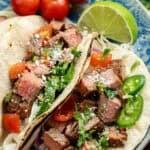 Carne Asada Tacos overhead image of carne asada tacos on a blue plate with a lime and tomatoes