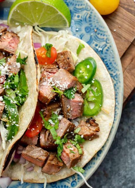 overhead image of two carne asada tacos on a blue plate with jalapenos