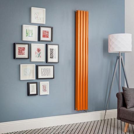 Milano x ECOSO Aruba electric sunset orange vertical designer radiator on blue wall nearby multiple framed pictures and large lamp by charcoal gray chair